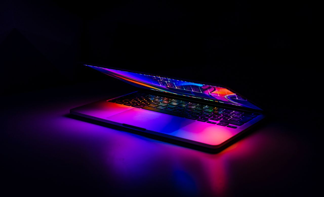 gallery-4 A partially closed MacBook with vibrant, colorful light reflections on a dark background.