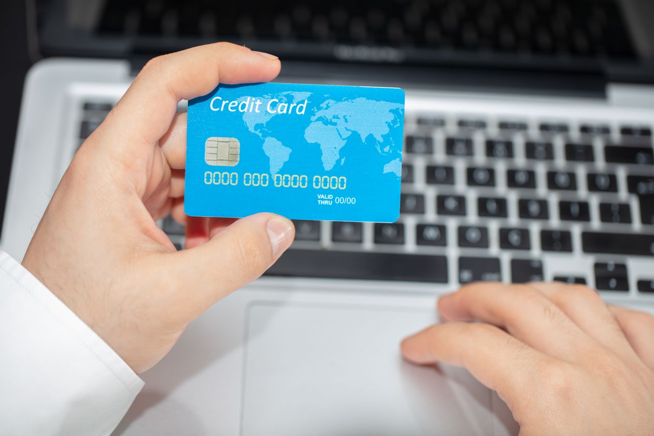 about-img Person holding credit card near laptop for online shopping, emphasizing secure online transactions.