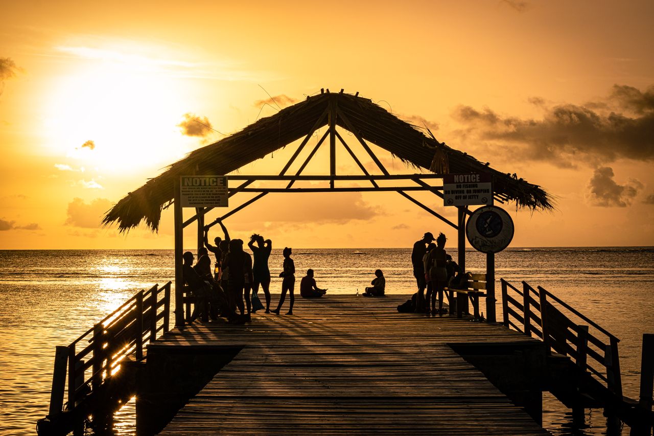 gallery-3 Silhouetted people gather on a tropical jetty during a breathtaking sunset in Western Tobago.