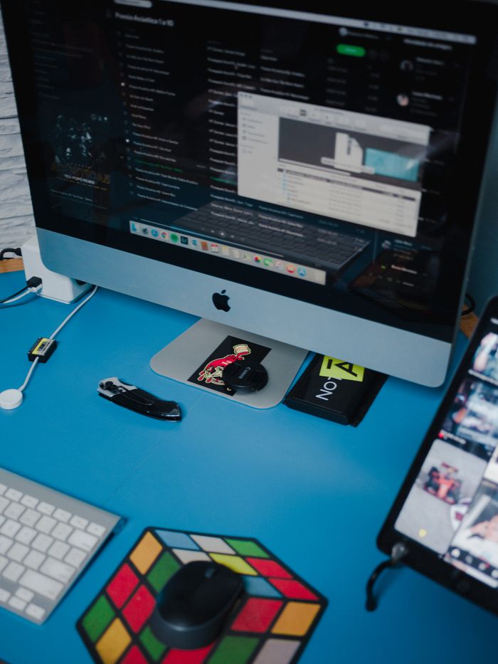 ours-journey A neat workspace setup with computer, gadgets, and a Rubik's cube on a blue desk.